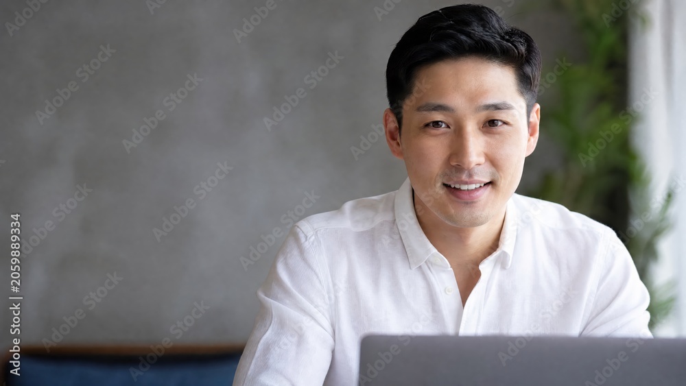 Obraz premium Generative AI, Smiling Asian businessman looking at camera while working on laptop at home office