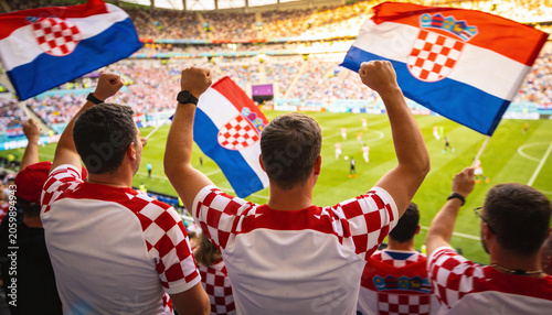 Cheering men raising Croatian flags while wearing red-and-white checkered jerseys in stadium stands