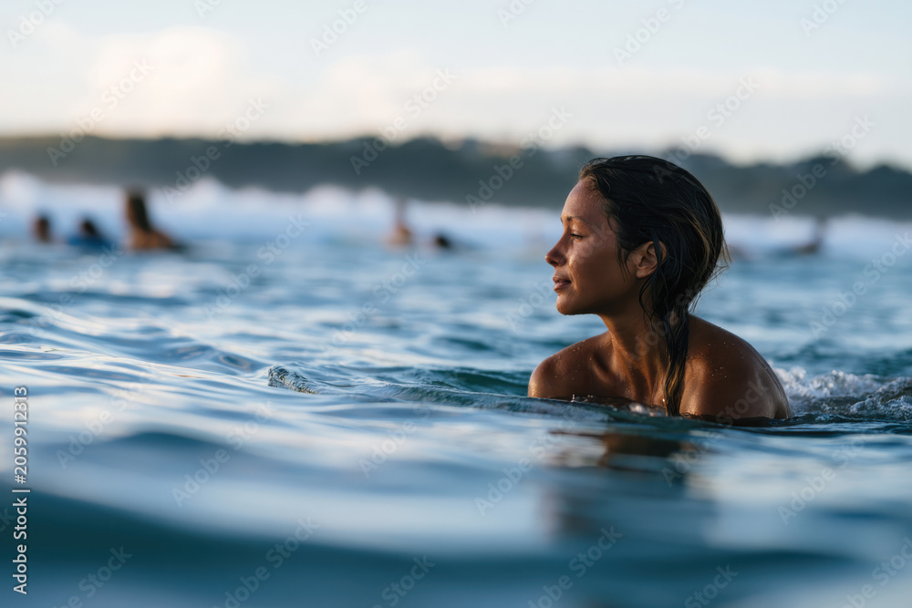Fototapeta premium A profile view of a determined woman swimming through the ocean waves, highlighting her strength and connection to the natural environment amidst a lively atmosphere.