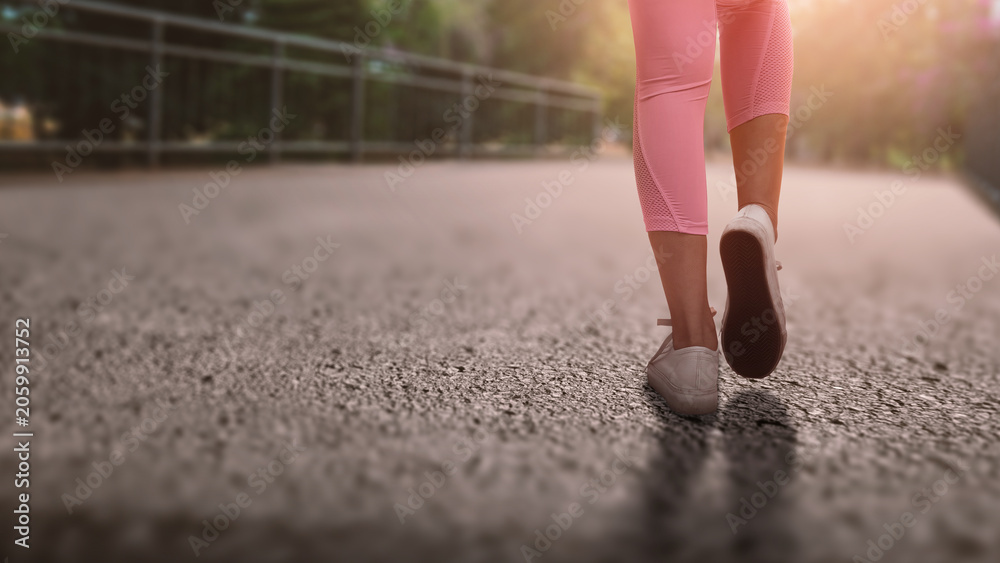 Naklejka premium A close-up, low-angle shot of a woman walking on an outdoor path, wearing pink leggings and white sneakers, capturing a sense of active lifestyle and motion