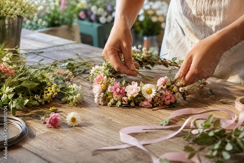 Fresh flower crown craft on table with anonymous hands