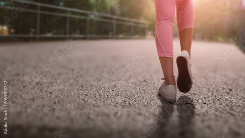 A close-up, low-angle shot of a woman walking on an outdoor path, wearing pink leggings and white sneakers, capturing a sense of active lifestyle and motion