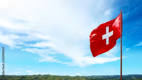 National flag of Switzerland waving on a flagpole against a scenic blue sky with clouds and hills