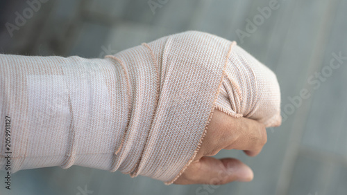 A patient suffering from a broken bone or muscle strain holding his wrapped wrist, representing workplace accidents, rehabilitation, health insurance and medical recovery. Selective focus.