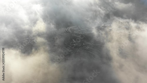 Drone flight over low hanging clouds and mist reveals amazing terraced rice fields in Yuanyang - idyllic rural landscape in China