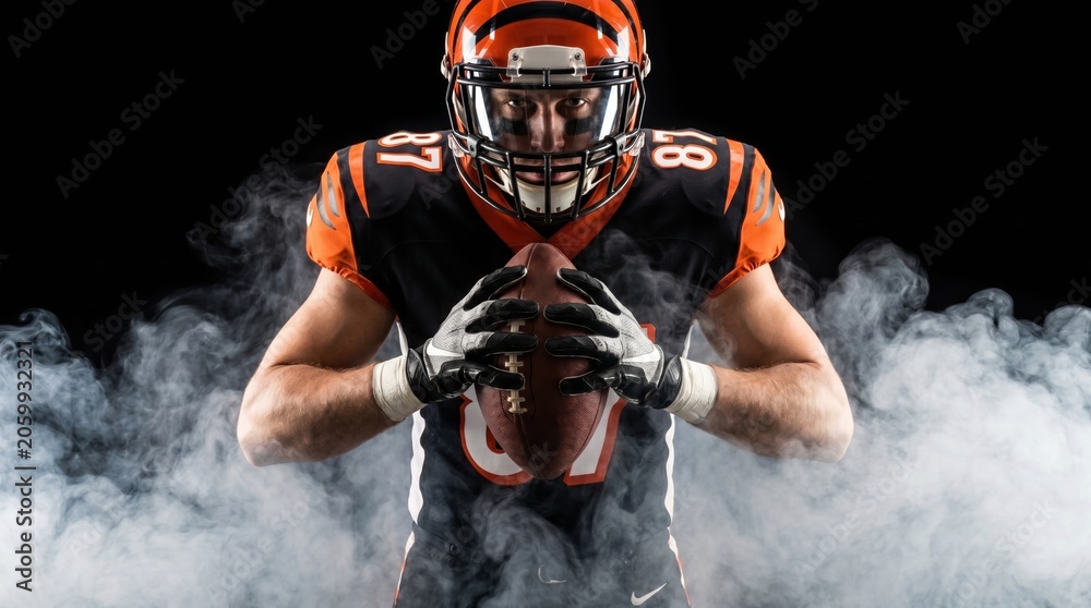 Obraz premium American football player on a dark background in smoke in black and orange equipment.