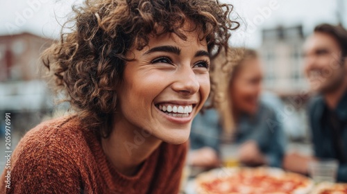 Young woman with curly hair laughing heartily with friends enjoying pizza outdoors