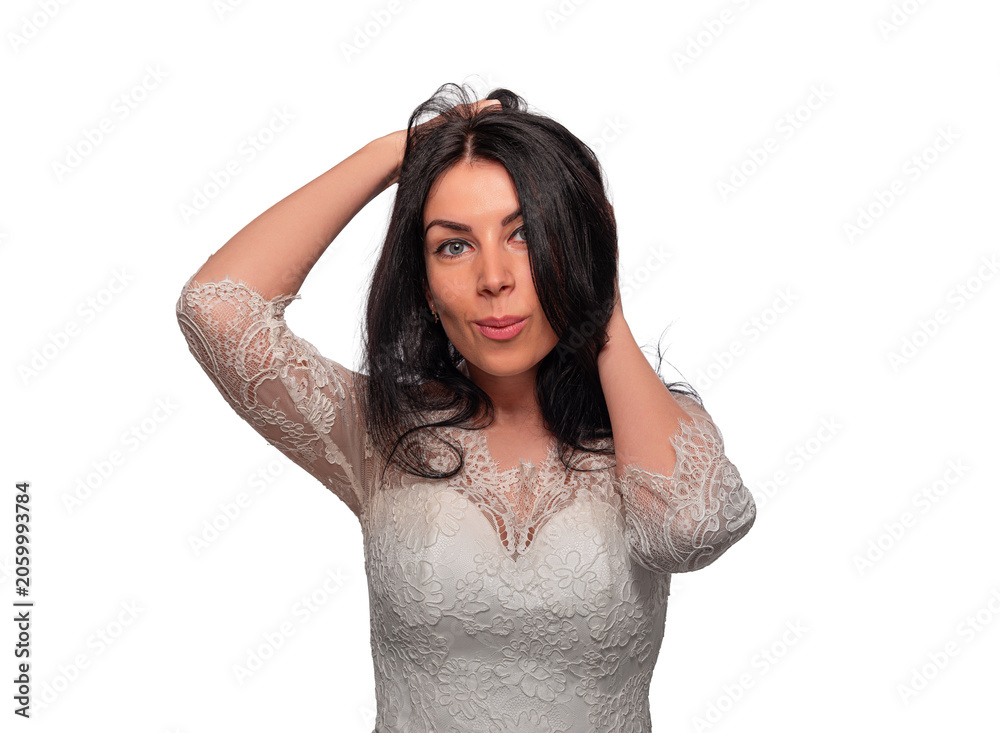 Naklejka premium A beautiful young woman with long dark hair wears an elegant white lace dress while running her hands through her hair against a plain white background.