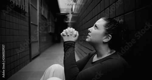 Woman sitting on floor in narrow corridor praying quietly, seeking help, hope amid despair, faith during hardship, emotional vulnerability and inner strength