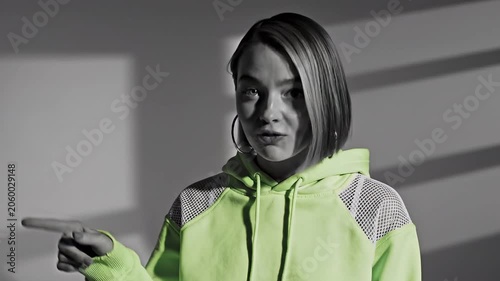 Young woman with short hair wearing a hoodie speaks and points to the side. Video sequence of casual communication and gesturing by a girl in interior setting.
