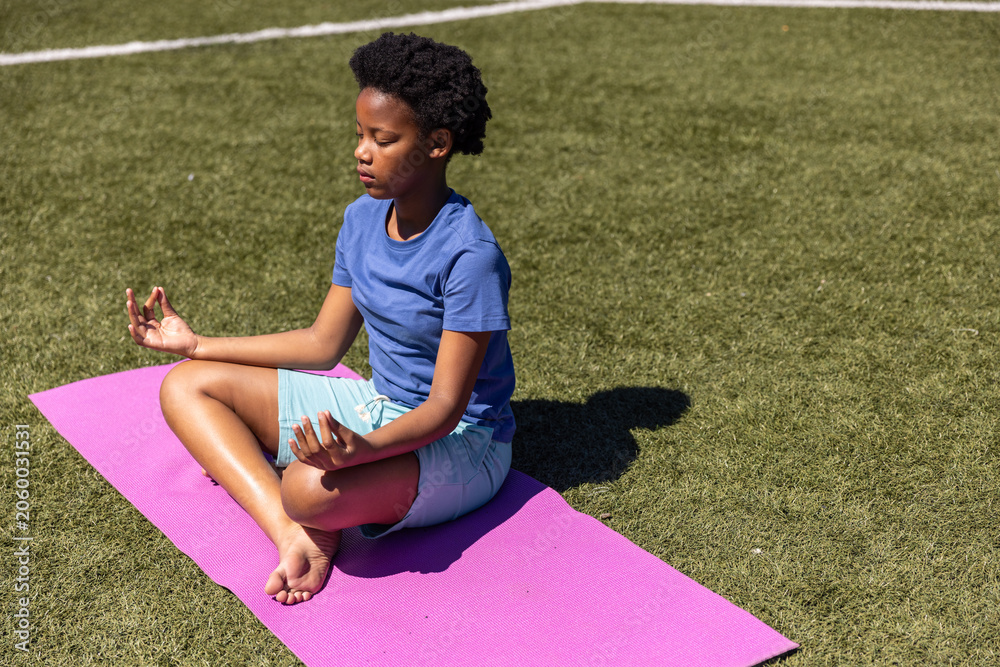 Obraz premium African American child meditating on pink mat on turf, in blue t-shirt, white line and shadow
