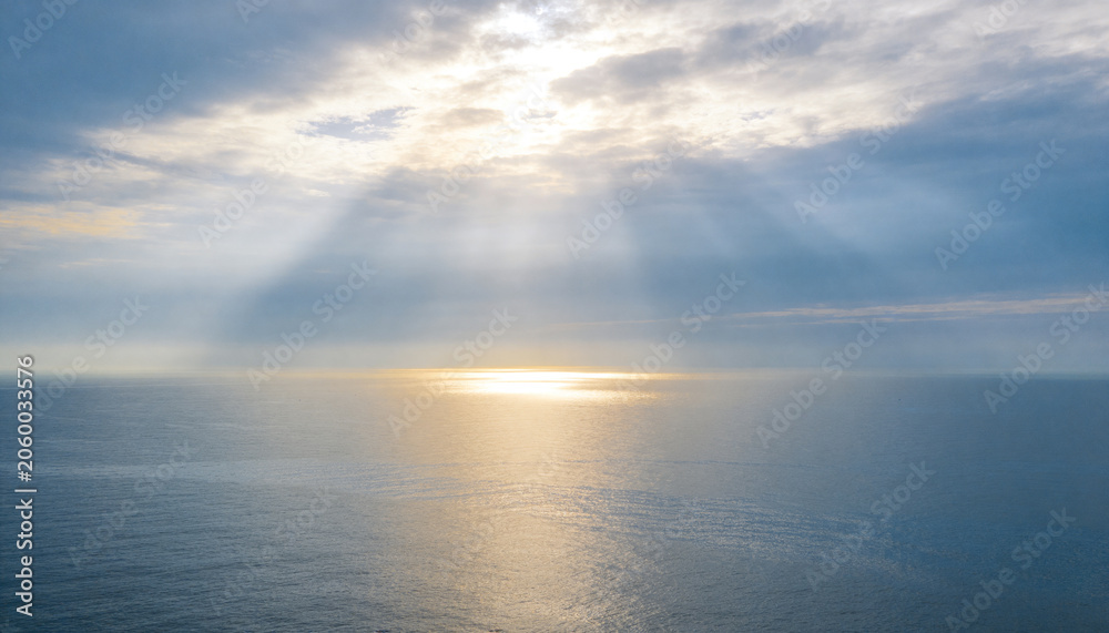 Obraz premium Showing sunlit ocean patch creating reflection over horizon at sea, with clouds and sunbeams