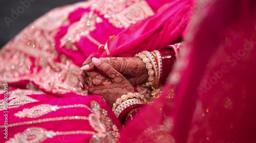 Close Up of Indian Bride Hands with Mehndi and Red Chooda Resting on Pink Lehenga