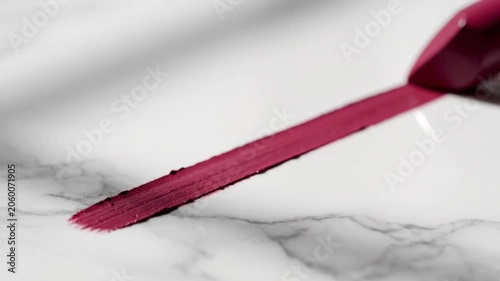 A detailed close-up shot of an unbranded matte dark red lipstick applying a rich streak of color across a luxurious polished white marble table. 