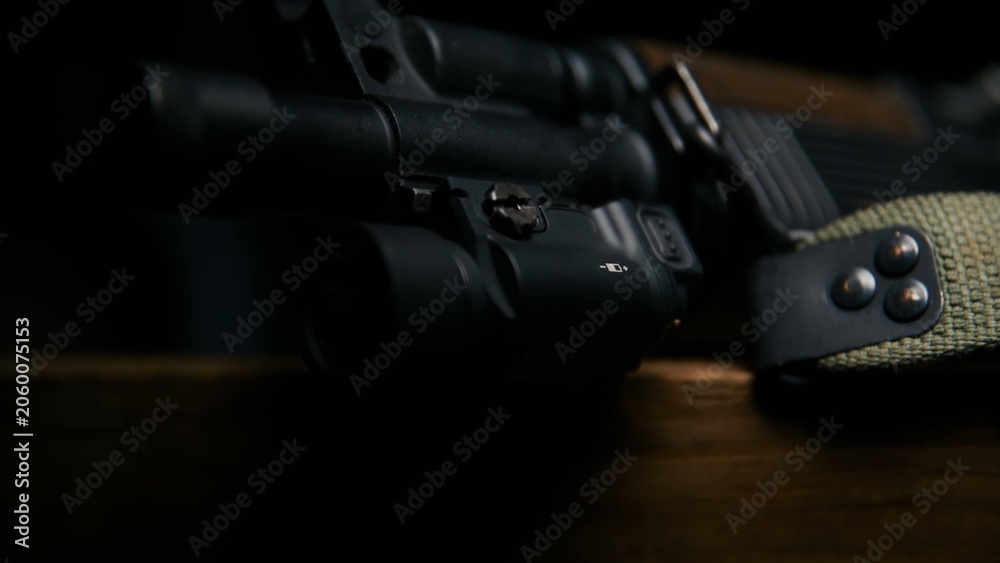 Obraz premium This close up captures the tactical flashlight secured to the barrel assembly of a firearm resting on a wooden surface emphasizing the matte finish and integrated design of the accessory