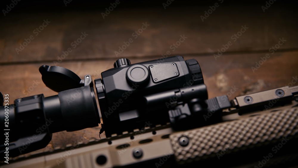 Obraz premium A side profile view of a tactical optic mounted on a tan textured rail platform highlighting the mechanical quick release lever and secure fastening hardware on professional weaponry