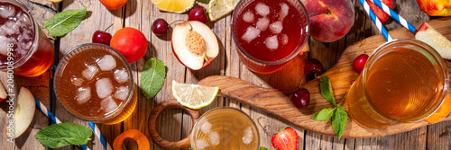 Summer refreshing drink, non alcohol tea based cocktails, iced tea varieties in different glasses, with fruit juices - strawberry, peach, apricot, cherry cold tea on wooden cozy background
