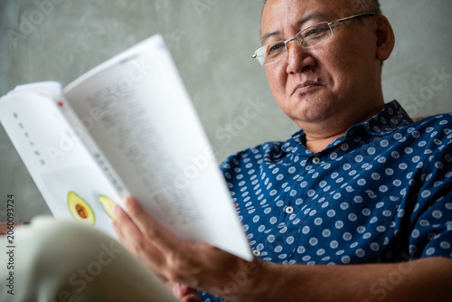 Foto Man in glasses reading a book, wearing a blue patterned shirt.