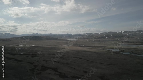 Low altitude drone flight forward along dirt road in melting spring mountain valley against snowy peaks. Travel journey. RAW flat profile uncorrected video footage.
