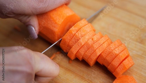 woman hands cutting carrots into round slices on wooden cutting board