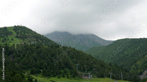 top of the mountain hidden by white rain clouds, chairlift lines on the hills, cloudy rainy weather