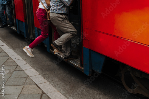 Billede på lærred Passengers step into a red tram at a city stop during daily travel