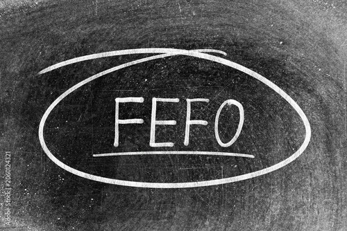 White chalk hand writing in word FEFO (Abbreviation of first expired first out)  and circle shape on blackboard background