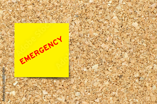 Yellow note paper with word emergency on cork board background with copy space