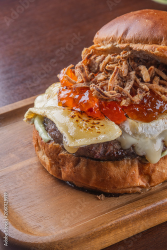 close up of flamed brie cheese on top of hamburger with pepper jelly and crispy onion