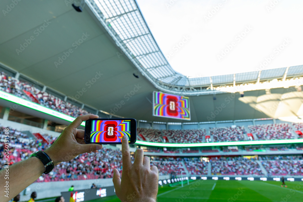 Naklejka premium MINSK, BELARUS JUNE 9, 2026: Man holding a purple Apple iPhone 14 Pro in the stadium. The official logo of the football World Cup in the USA, Mexico, and Canada.