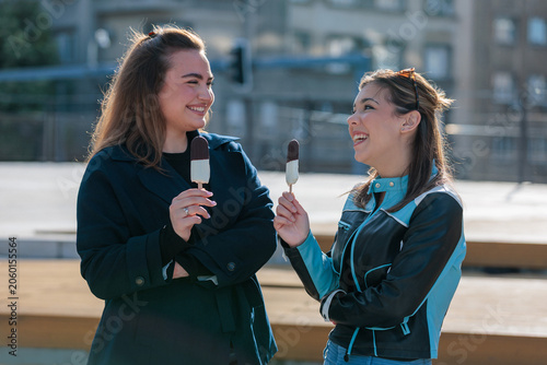 Two young women enjoy ice cream outdoors on a sunny day