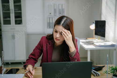 Young Asian businesswoman feeling frustrated and stressed, having a headache while using a laptop for work in a modern office