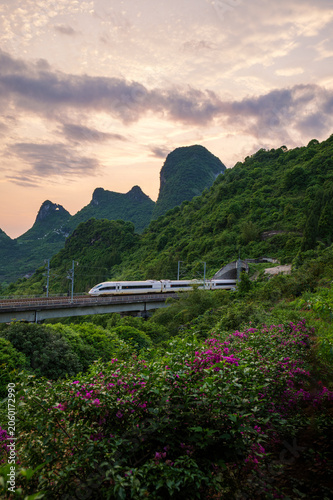 High-speed train crossing viaduct in lush karst mountains at sunset in Guangxi, China