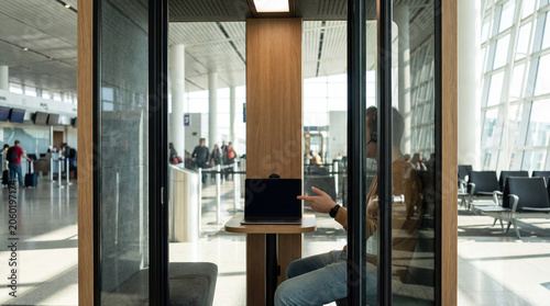Passenger works inside airport quiet pod with laptop headset showing private call remote meeting productivity during layover for business travel content commercial marketing visuals