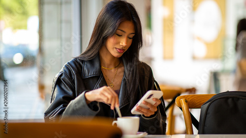 Foto Woman using smartphone while stirring coffee in cafe