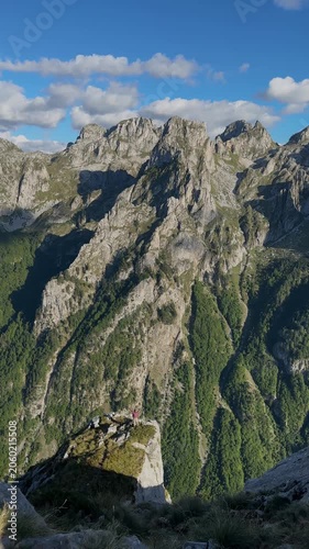 Scenic view of dramatic rocky cliffs in Plav Gusinje, Montenegro, with a tiny distant person standing on a peak with outstretched arms in a vast mountain landscape
