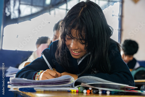 Foto Young girl student smiling while writing in notebook at school