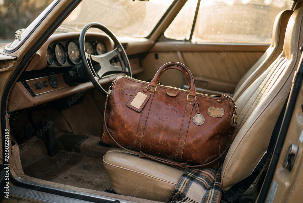 Obraz premium Brown leather duffel bag with football on it on tan seat in classic car