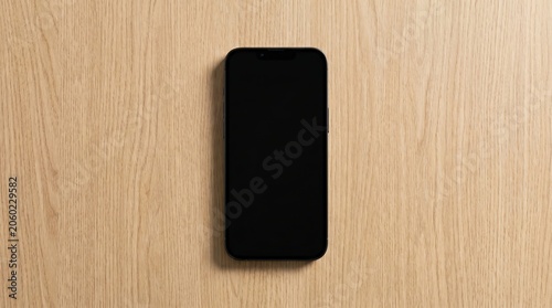 Smartphone with black screen lying flat on light brown wooden table surface in minimalist overhead view for digital mockup and technology presentation.
