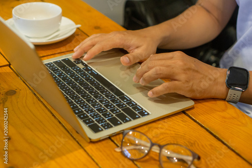 Close-up of businessman hands typing on laptop keyboard at wooden desk.