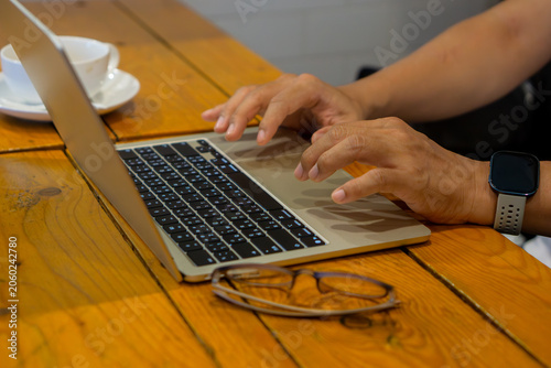 Eyeglasses on wooden table in front of businessman working on laptop.