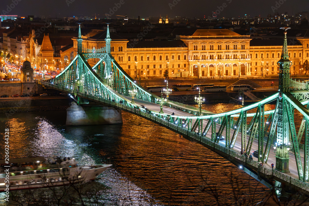 Naklejka premium Illuminated panoramic view of a Liberty bridge crossing the Danube River through historic downtown Budapest Hungary dramatic European architecture night cityscape travel landmark