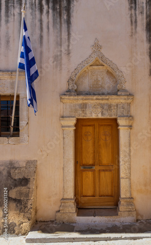 Architectural close-up detail of the traditional entrance door of Zoodochos Pigi church featuring the Greek national flag in Gouves, Crete, Greece