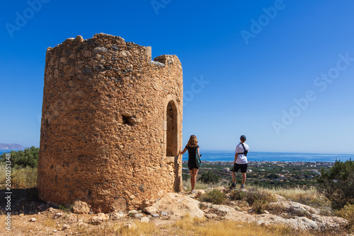 Mother and young son with an arm brace standing at the Gournes Gouvon rotunda viewpoint, looking down at Kato Gouves village and the sea in Crete, Greece