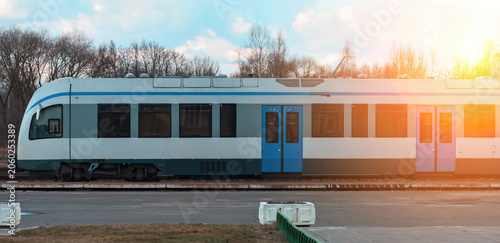 Train stops at station during bright afternoon in a rural area with trees in the background and clear sky