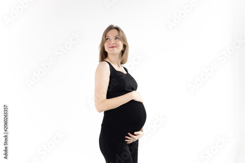 Happy pregnant woman in black outfit cradling her belly, looking up and smile on white background.