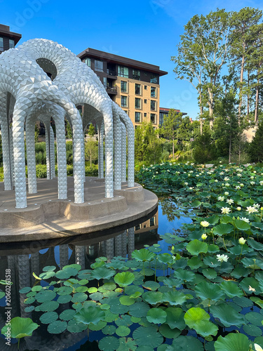 A modern public art installation overlooks a blooming lotus pond at Downtown Cary Park, blending contemporary design with landscaped gardens in Cary, North Carolina.