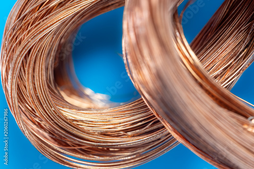 High quality copper wire coils on a blue background. Close up of bright copper wire for electrical industry. Shiny metallic copper wire cable components for energy.