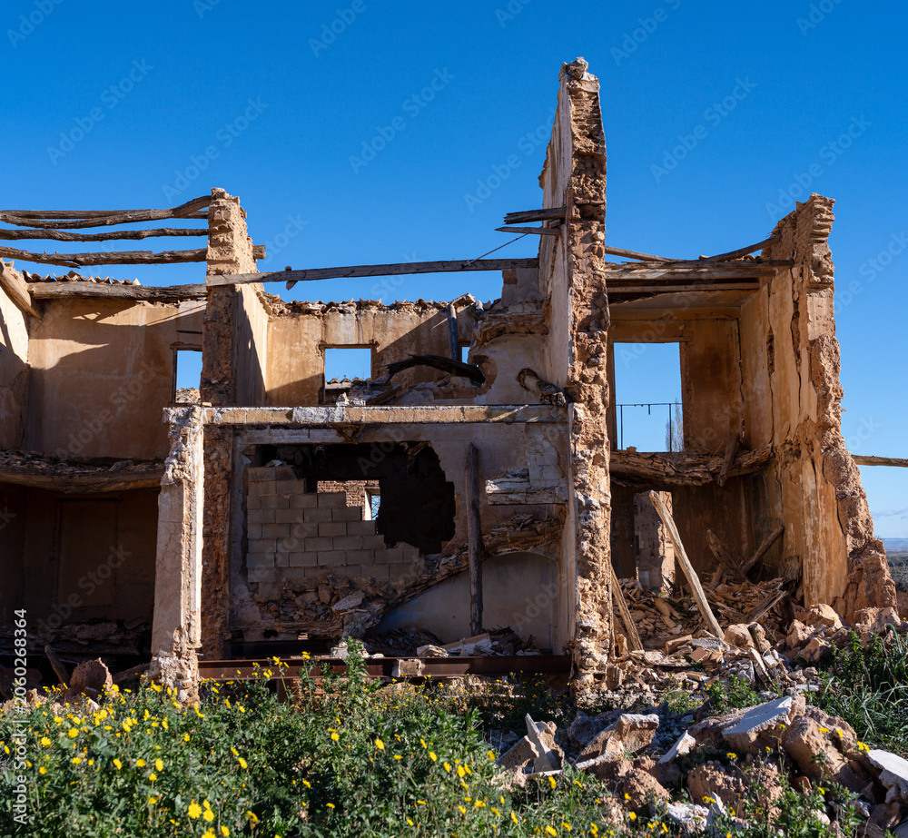 Fototapeta premium Destroyed historic building with exposed wooden beams and rubble in the old town ruins of Belchite under a blue sky