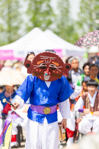Korean traditional mask dance performance at an outdoor festival with colorful costumes and audience in the background.